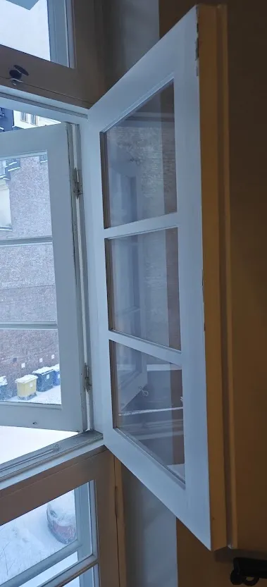 Avoin valkoinen ikkuna, jossa on useita ruutuja, näyttää ulos lumiseen maisemaan, mikä voi vaatia ikkunan huoltoa.
