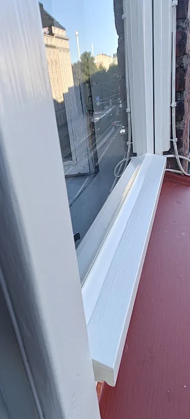 Valkoinen ikkunanpoka ja ikkunalauta heijastavat kaupunkinäkymää kadulle ja rakennuksiin, kuvaten kunnostettua ikkunaa.