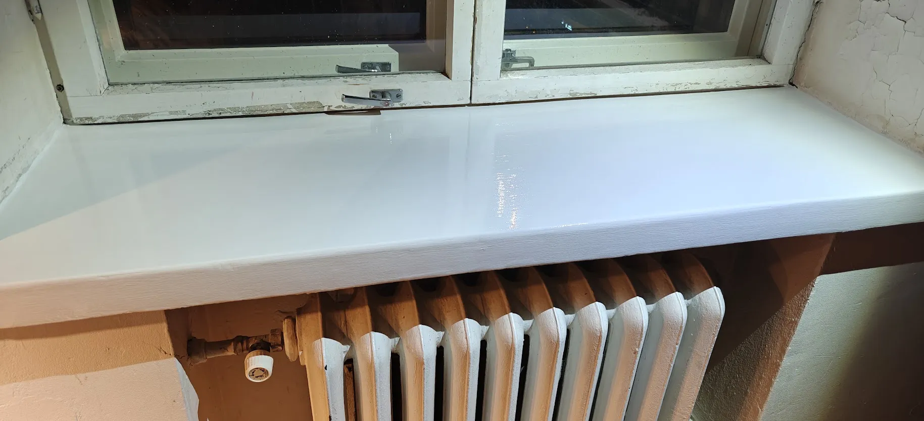 Valkoinen ikkunalauta ja ikkuna, jonka karmit kaipaavat kunnostusta.