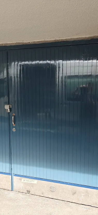 Pystypaneeleista koostuva sininen autotallin ovi, jonka väri liukuu tummasta vaaleaan, on kunnostettu ja maalattu.