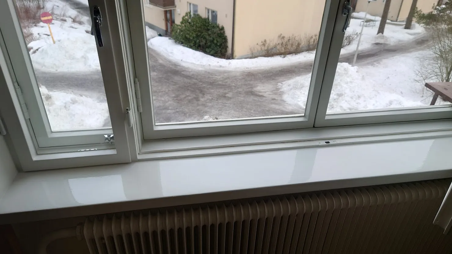Valkoinen, huollettu ikkuna ja ikkunalauta, josta avautuu näkymä lumiseen pihaan.